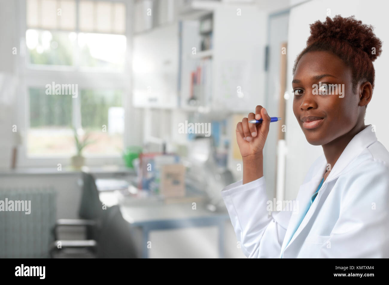 African scientist, medical or or graduate student. Bright, confident young woman wearing lab coat holds a pen in a doorway of her office. Stock Photo