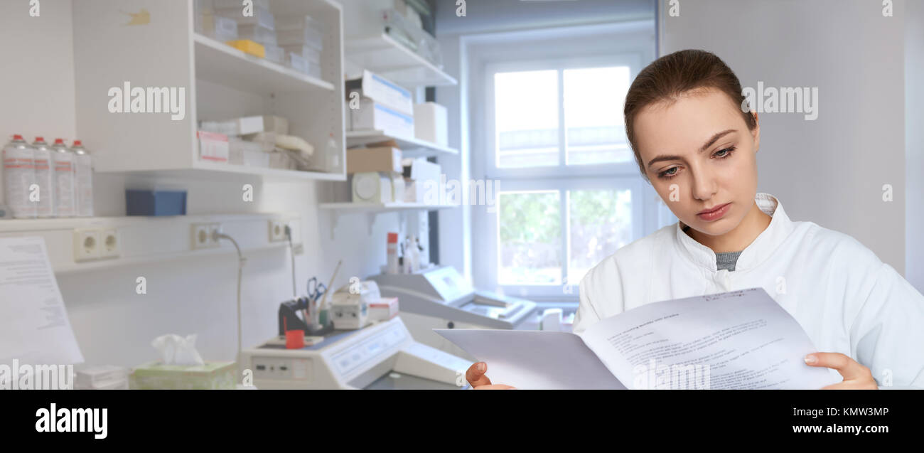 Panoramic image of a young female scientist reading printed notes in scientific laboratory Stock Photo