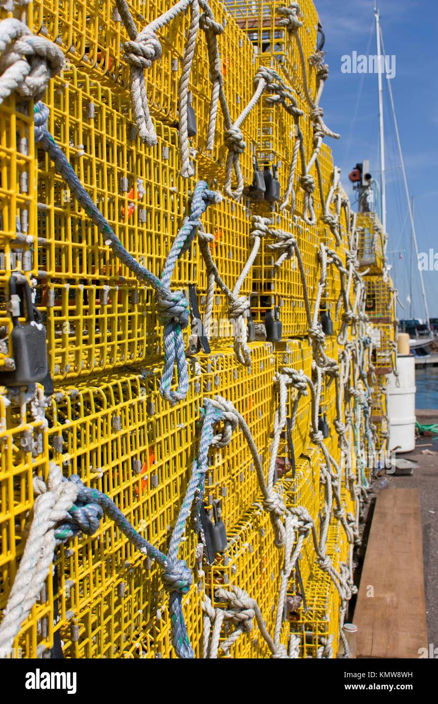 Large stack of yellow commercial lobster traps with a boats mast in the