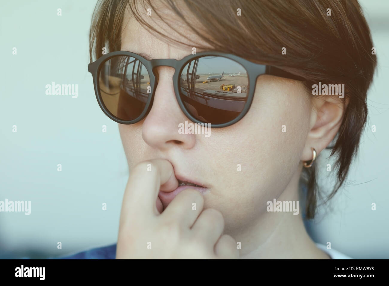 A woman is afraid to fly. She looks at the plane with fear. Focus on sunglasses reflection Stock Photo