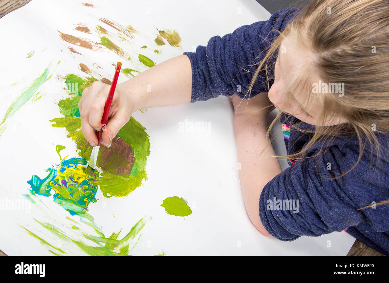 young child playing with paint brush in splattered paint on a white background Stock Photo