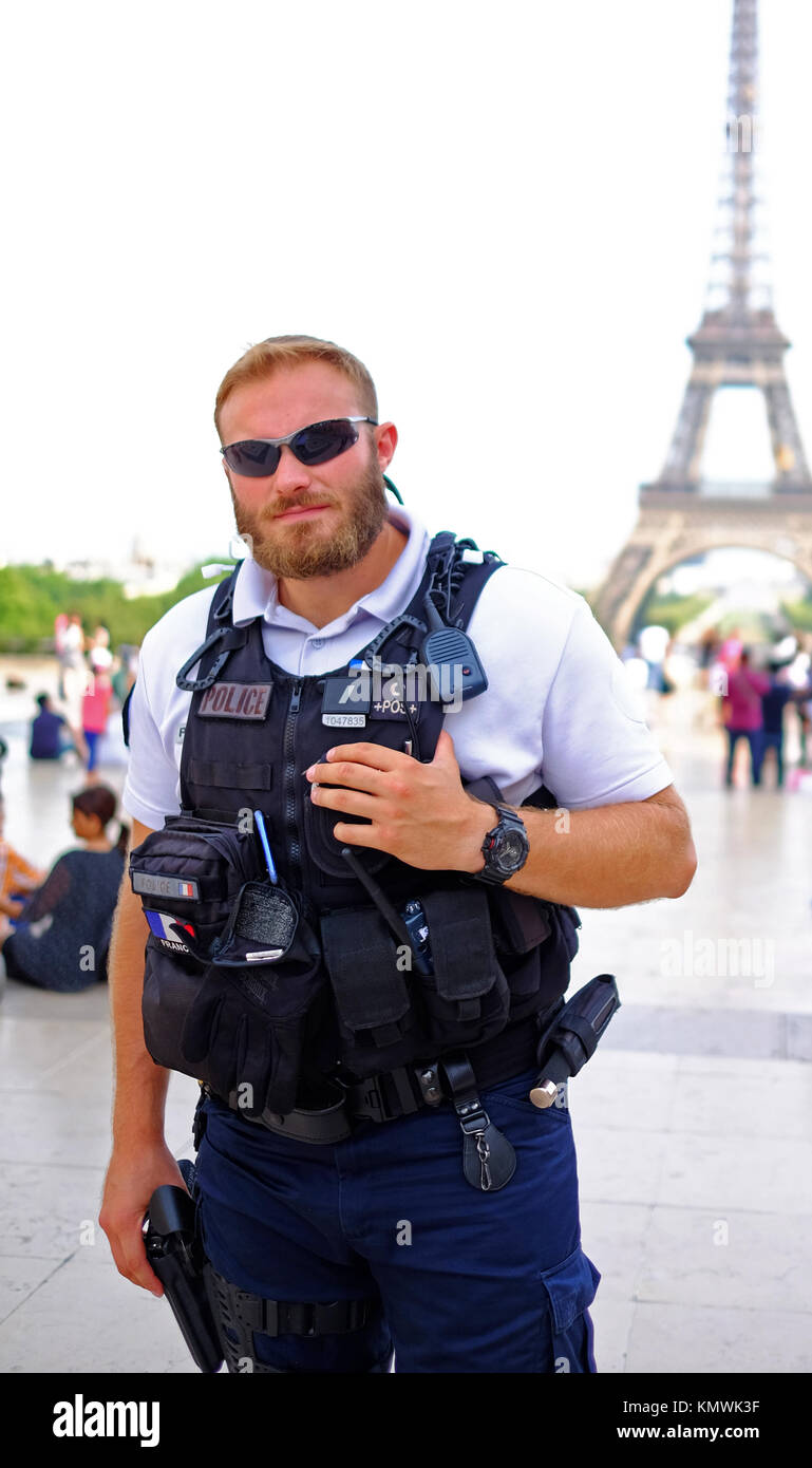 An armed policeman remains alert while his photo is taken, his hand is on his gun, while on patrol among tourists at the Eiffel Tower in Paris Stock Photo