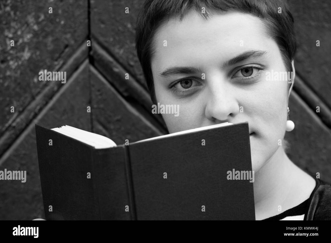 A Girl With Big Eyes And Short Hair Hides Behind A Book Close Up