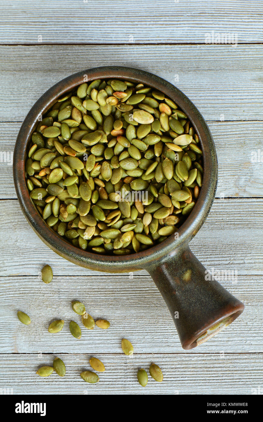 Raw pumpkin seeds in earthenware bowl on grey wooden background in vertical format.  Shot from overhead in natural light. Stock Photo