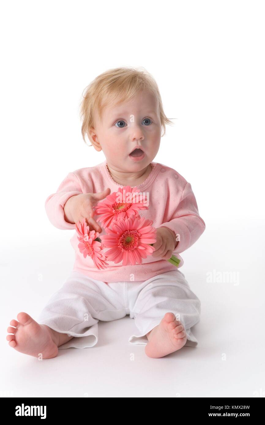 Baby Girl Is Sitting On The Floor With Pink Flowers Stock Photo