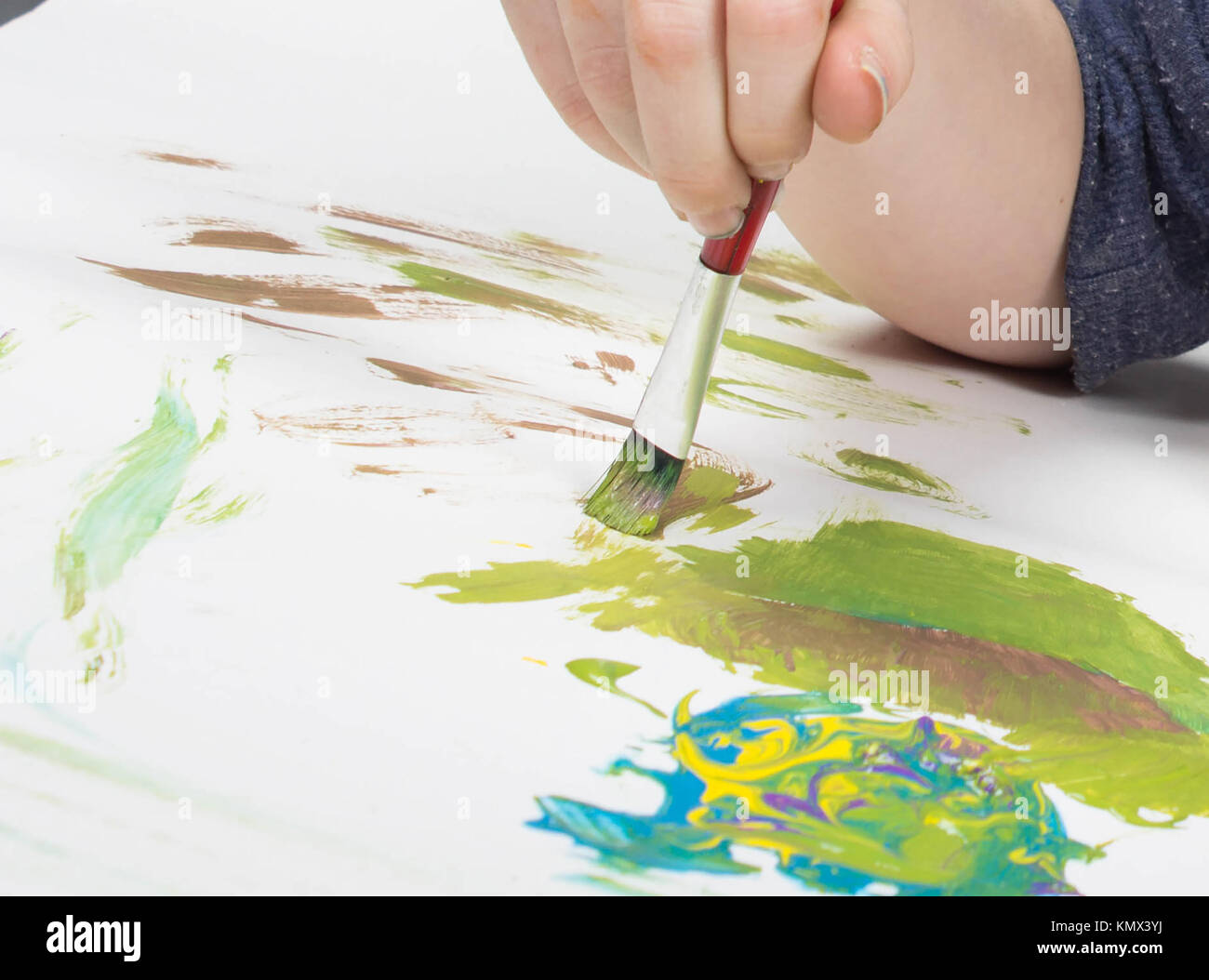 young child playing with paint brush in splattered paint on a white background Stock Photo