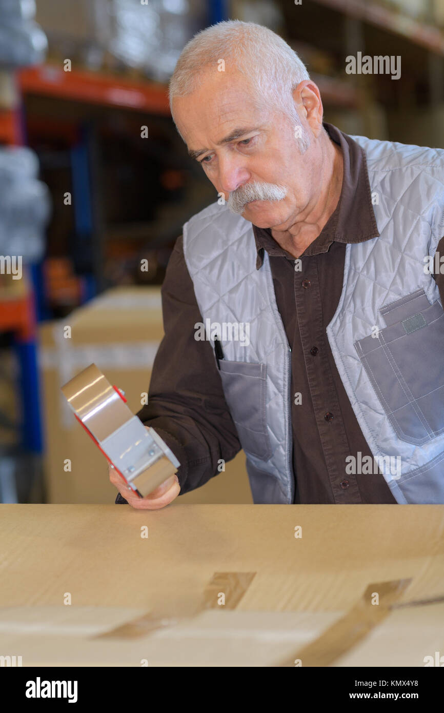 Senior man sealing cardboard box with a tape dispenser Stock Photo - Alamy