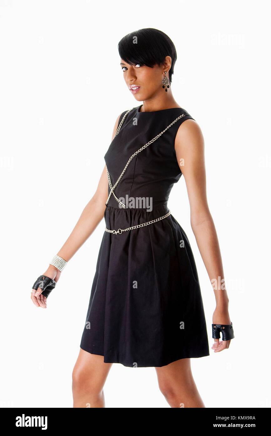 Beautiful modern classy African American female fashion model in black dress with silver chains and black biker gloves walking, isolated Stock Photo