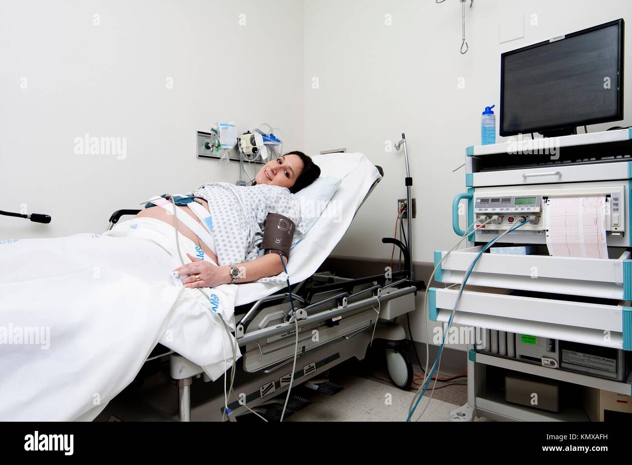 Pregnant Caucasian Hispanic Latina woman laying in a hospital gurney bed in the triage unit doing a medical non stress test NST while being hooked up Stock Photo