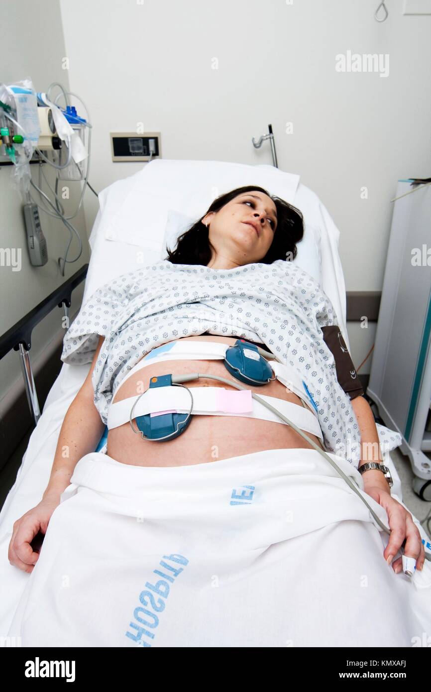 Pregnant Caucasian Hispanic Latina woman laying in a hospital gurney bed in the triage unit doing a medical non stress test NST while being hooked up Stock Photo