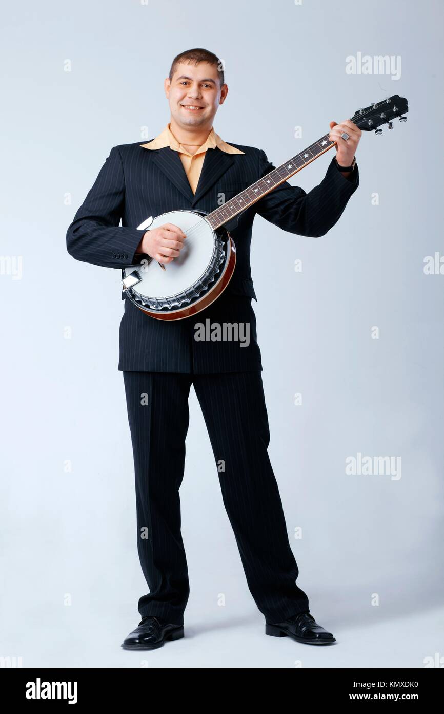Man in suite is standing and playing on banjo against white, full length Stock Photo
