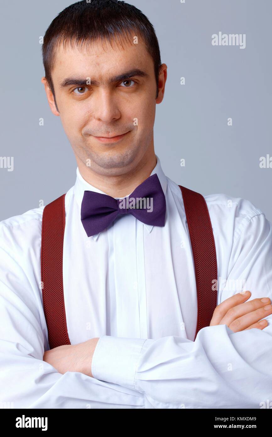 Man with purple bow tie and braces standing with his arms folded Stock