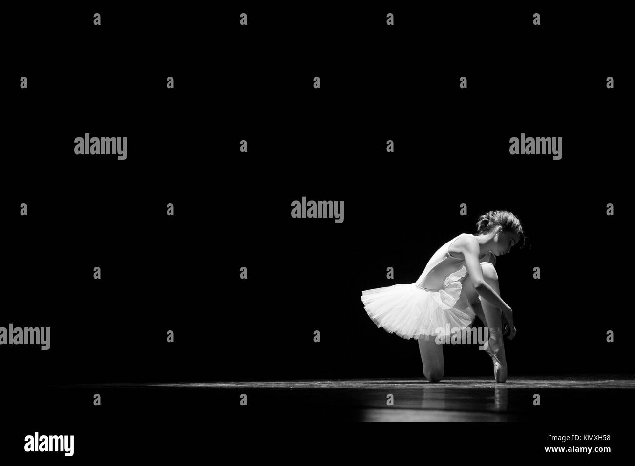 Young female ballet dancer tying ballet shoes before performing Stock