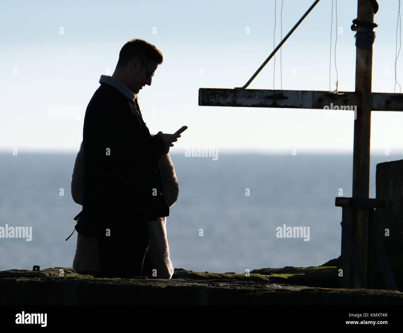 Man in silhouette on pier at seaside resort using  mobile phone. Stock Photo