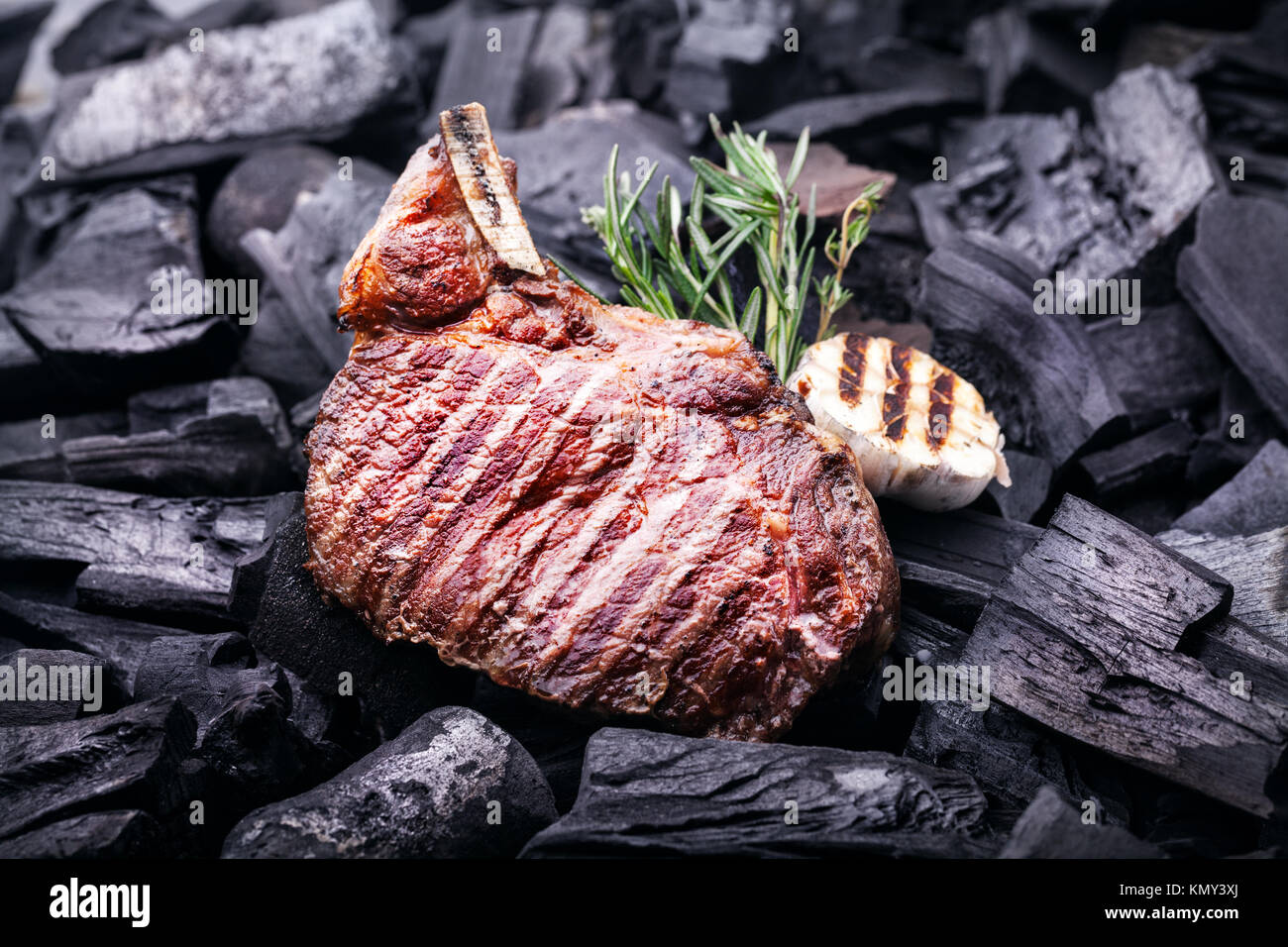 Grilled meat steak with garlic and rosemary on black coals at barbeque cookout Stock Photo