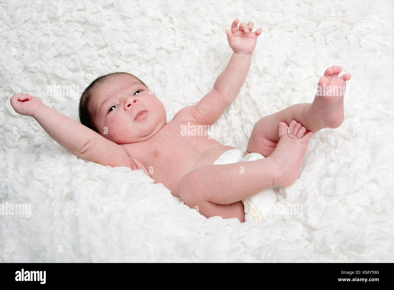 Happy Caucasian Hispanic infant baby falling on soft white cotton cloud with arms and legs in the air Stock Photo