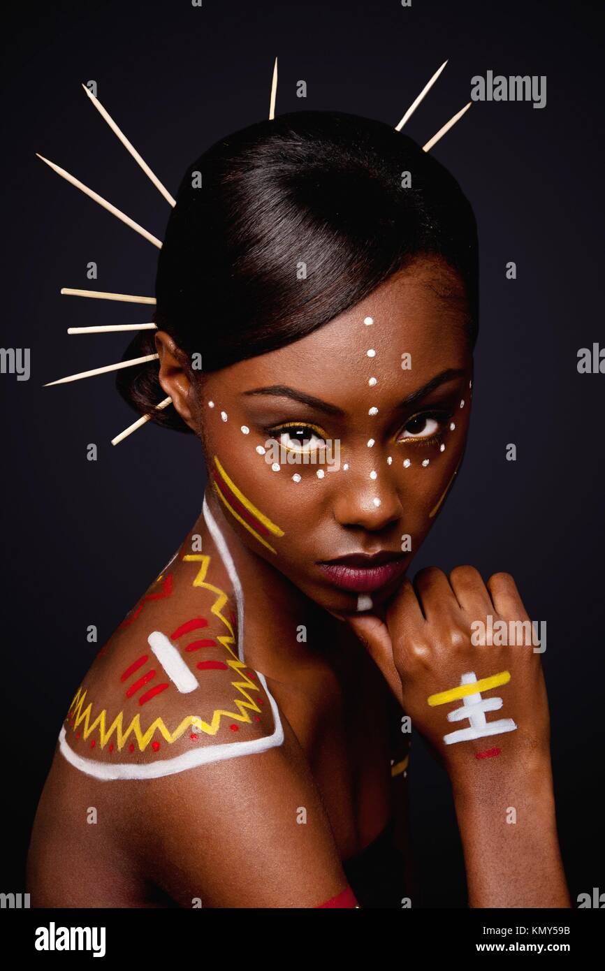 Beautiful exotic African female fashion face with tribal yellow red and  white makeup cosmetics and sticks in hair Stock Photo - Alamy