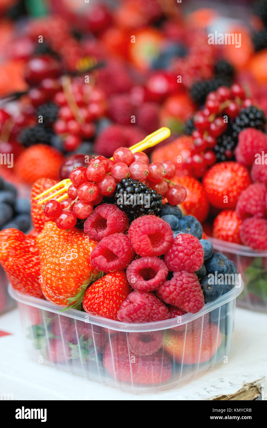 Mix of fresh ripe berries raspberry, strawberry, blackberry and blueberry in plastic boxes with disposable fork in market Stock Photo