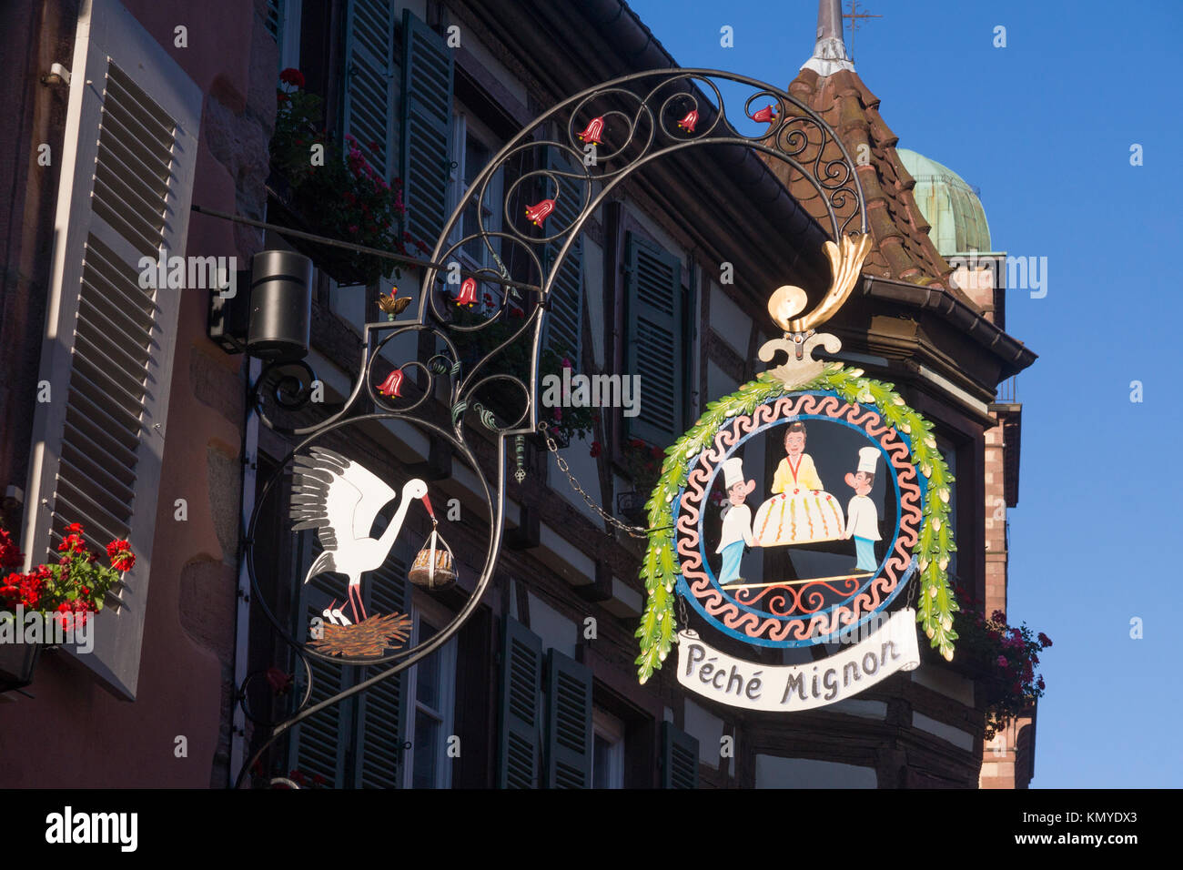Hanging shop sign for a patisserie, 'Péché Mignon (sweet sins) in Kayserberg, Alsace. The stork kougelhopf are a regional symbols of Alsace Stock Photo