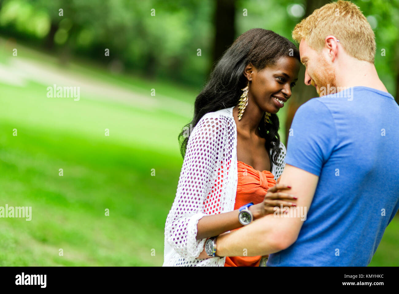 Stylish cute brunette girl sitting between legs of her boyfriend with beard  close to each other on the grass in the park in Spain in the evening, and  they both laughing Stock