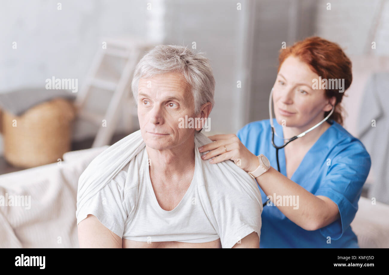 Cheerful nurse with stethoscope listening to lung sounds of patient