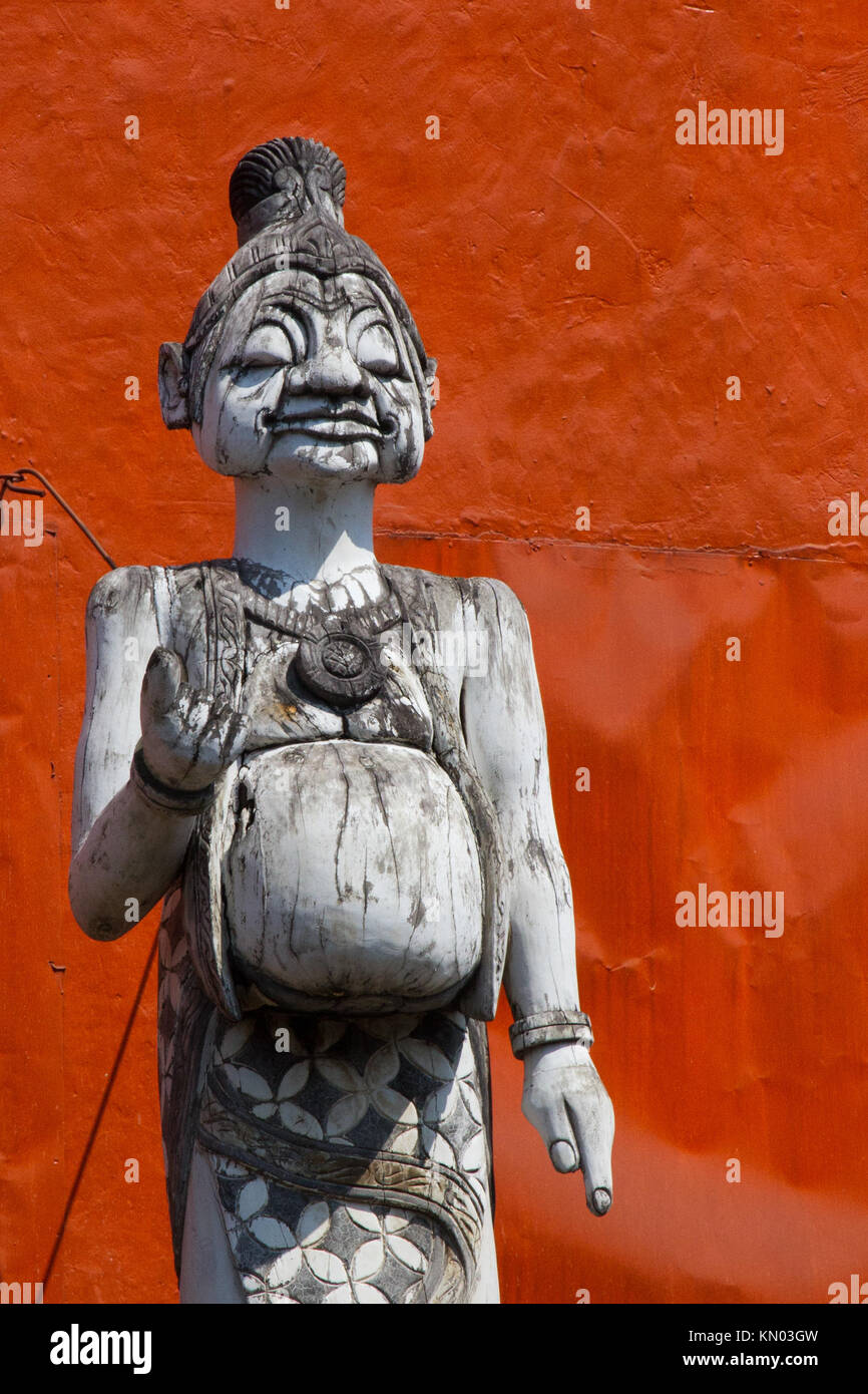 Carved Figure on top of building against bright red wall, Yogyakarter, Indonesia Stock Photo