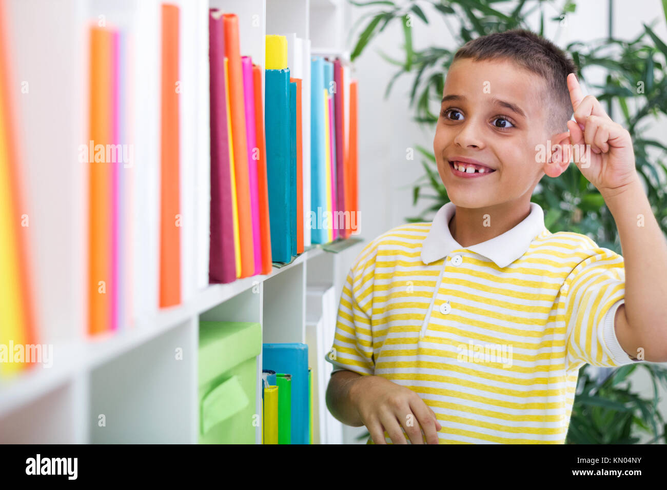 little boy standing next to a bookcase in the library Stock Photo