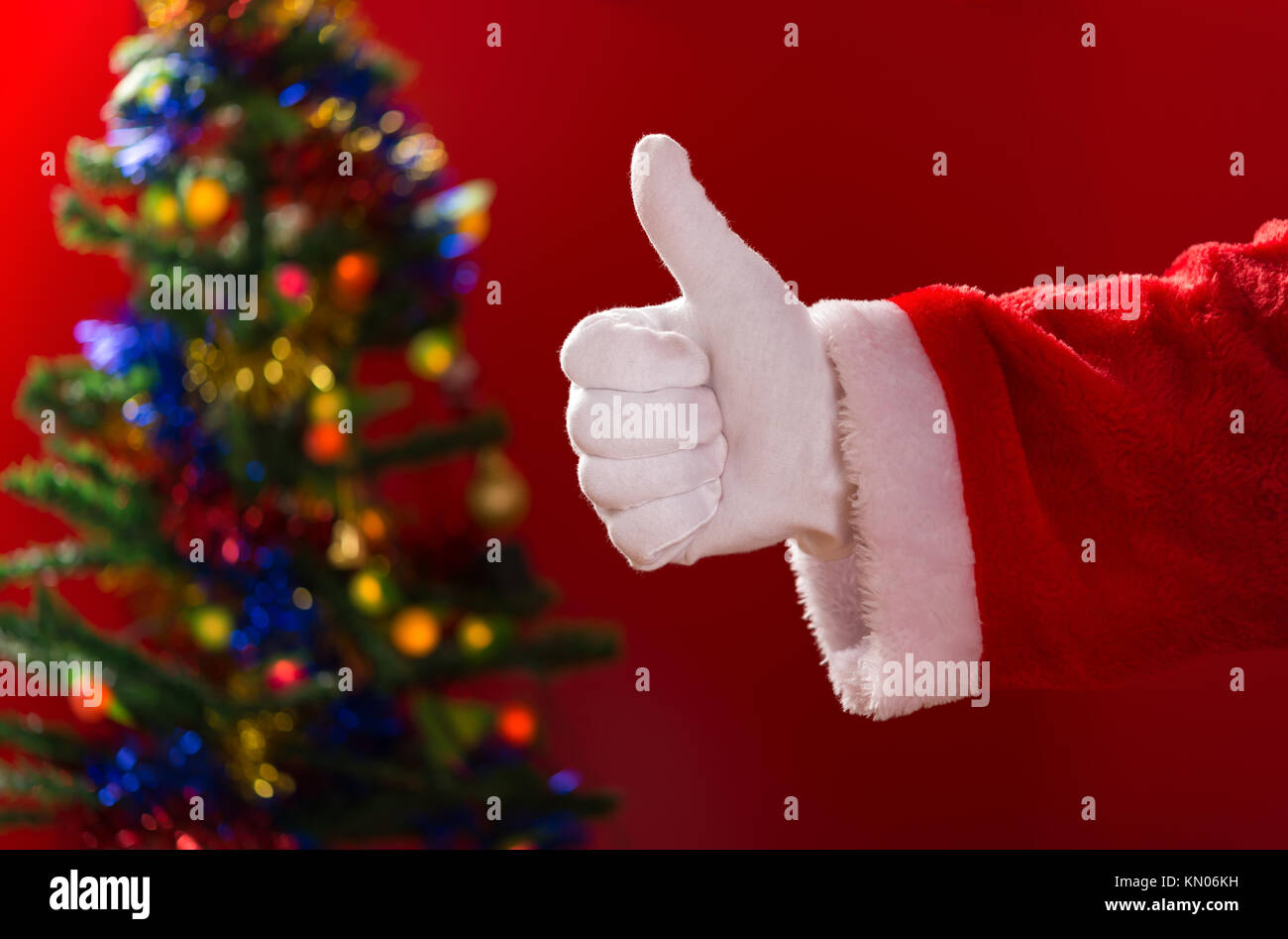 Santa Claus doing a thumbs up gesture with decorated Christmas tree on