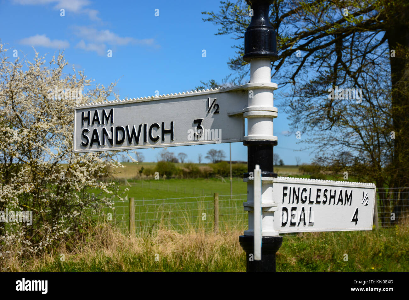 Amusing funny old fashioned signpost for Ham Sandwich, Finglesham and Deal in Kent, England with blue sky, sunshine and green field behind Stock Photo