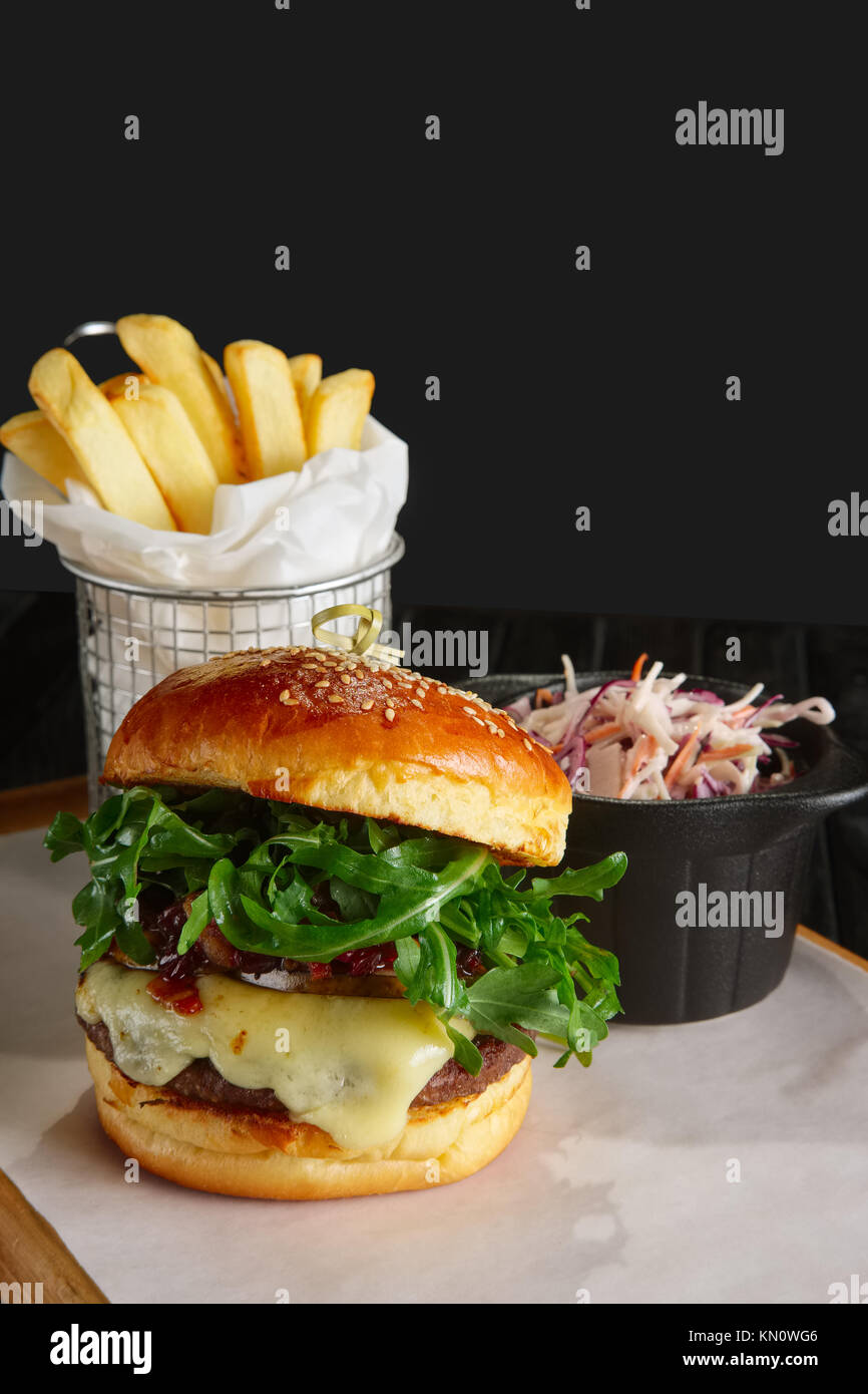 Juicy beef burger with lingonberry sauce, melted cheese, arugula served with fried potato and red cabbage Stock Photo