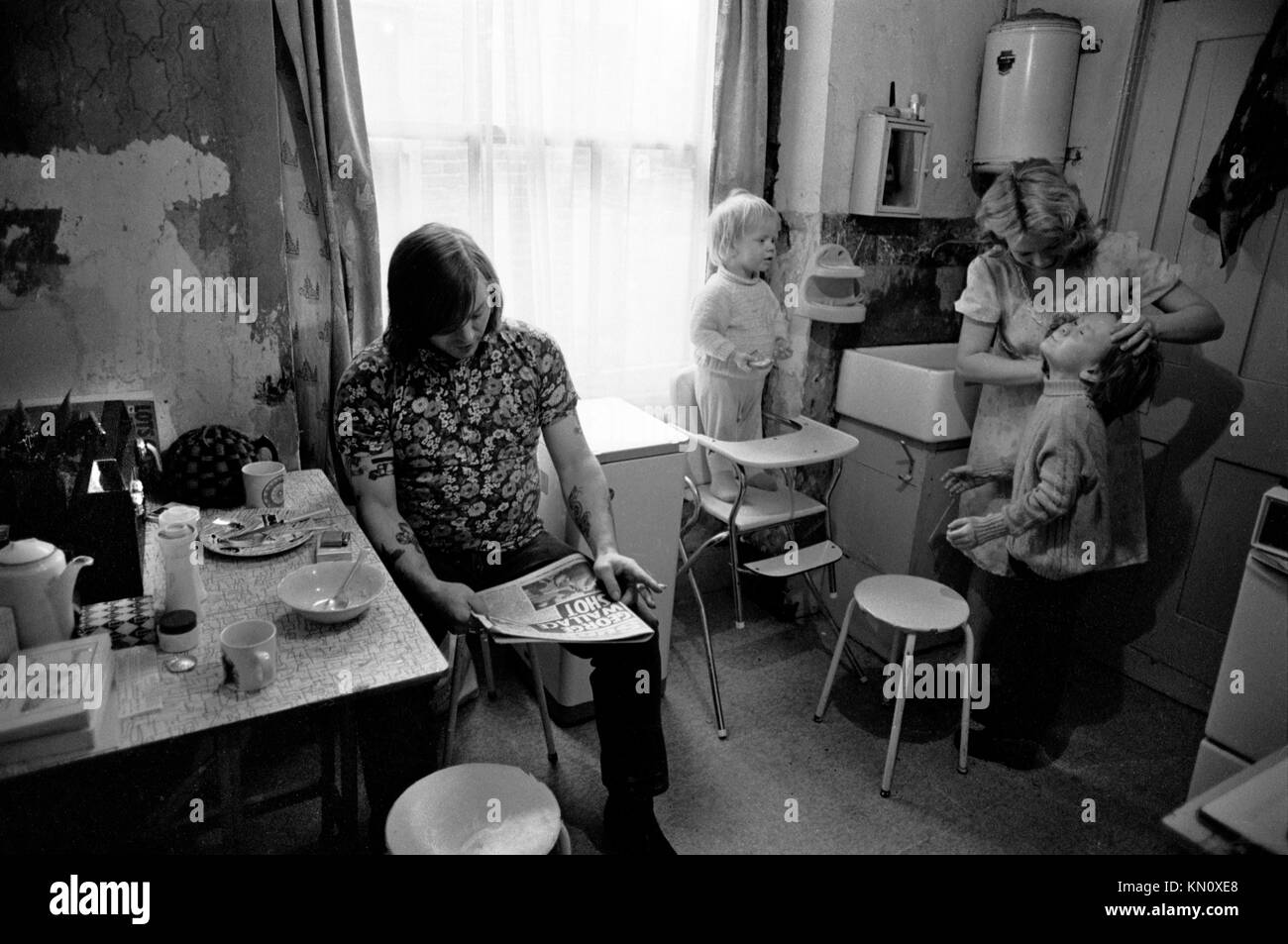 1970s Slum housing, kitchen doubles as bathroom. Family eating together. Poverty.  Ascot gas water heater on the the wall above the butler sink 1972  Fulham, London, England 70s UK HOMER SYKES Stock Photo