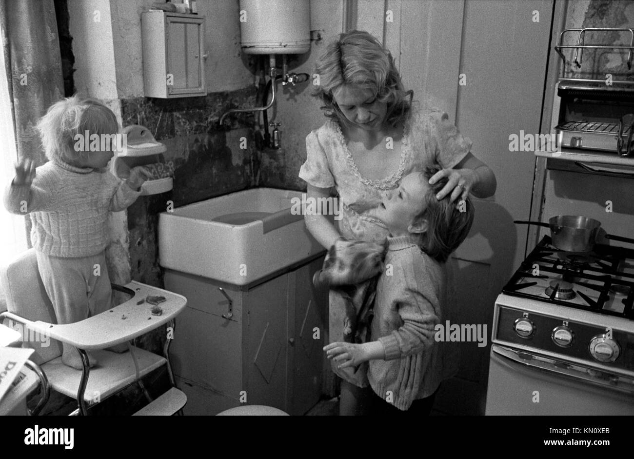 Slum housing, kitchen doubles as bathroom, getting washed by mother in the morning.1970s England. Ascot gas water heater on the the wall above the butler sink 1972  Fulham, London, England 70s UK HOMER SYKES Stock Photo