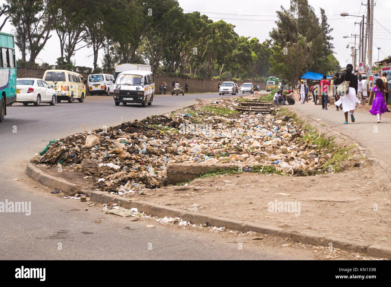 A large pile of plastic and general waste rubbish lies by the side of a busy road as vehicles drive past and pedestrians walk by, Nairobi, Kenya, East Stock Photo