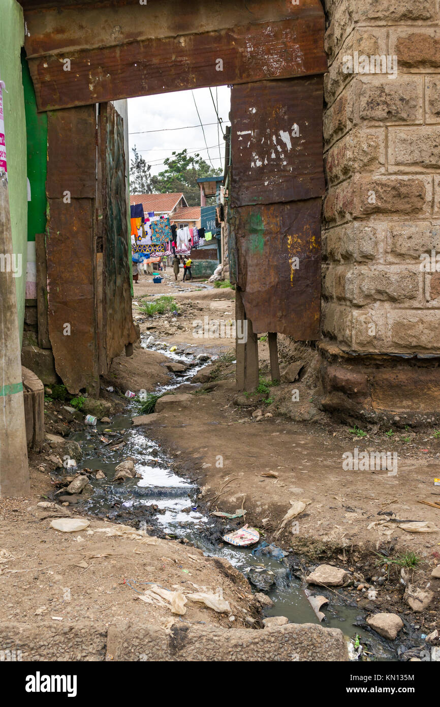 Waste water flows freely through an exterior doorway with a courtyard showing, children and people can be seen in the background, Huruma, Nairobi Stock Photo