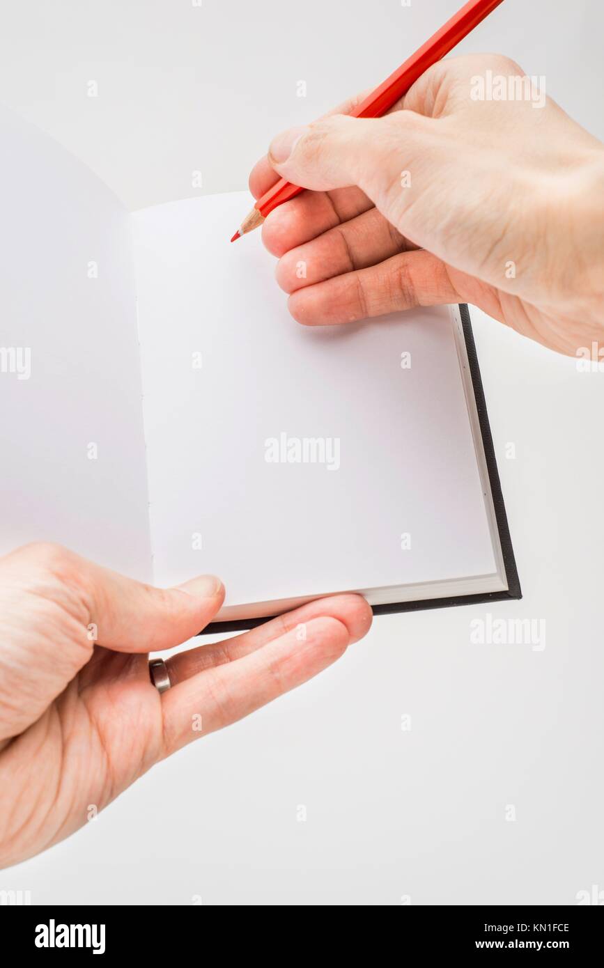 Closeup on white background of male hand holding blank note pad and red pencil. Stock Photo