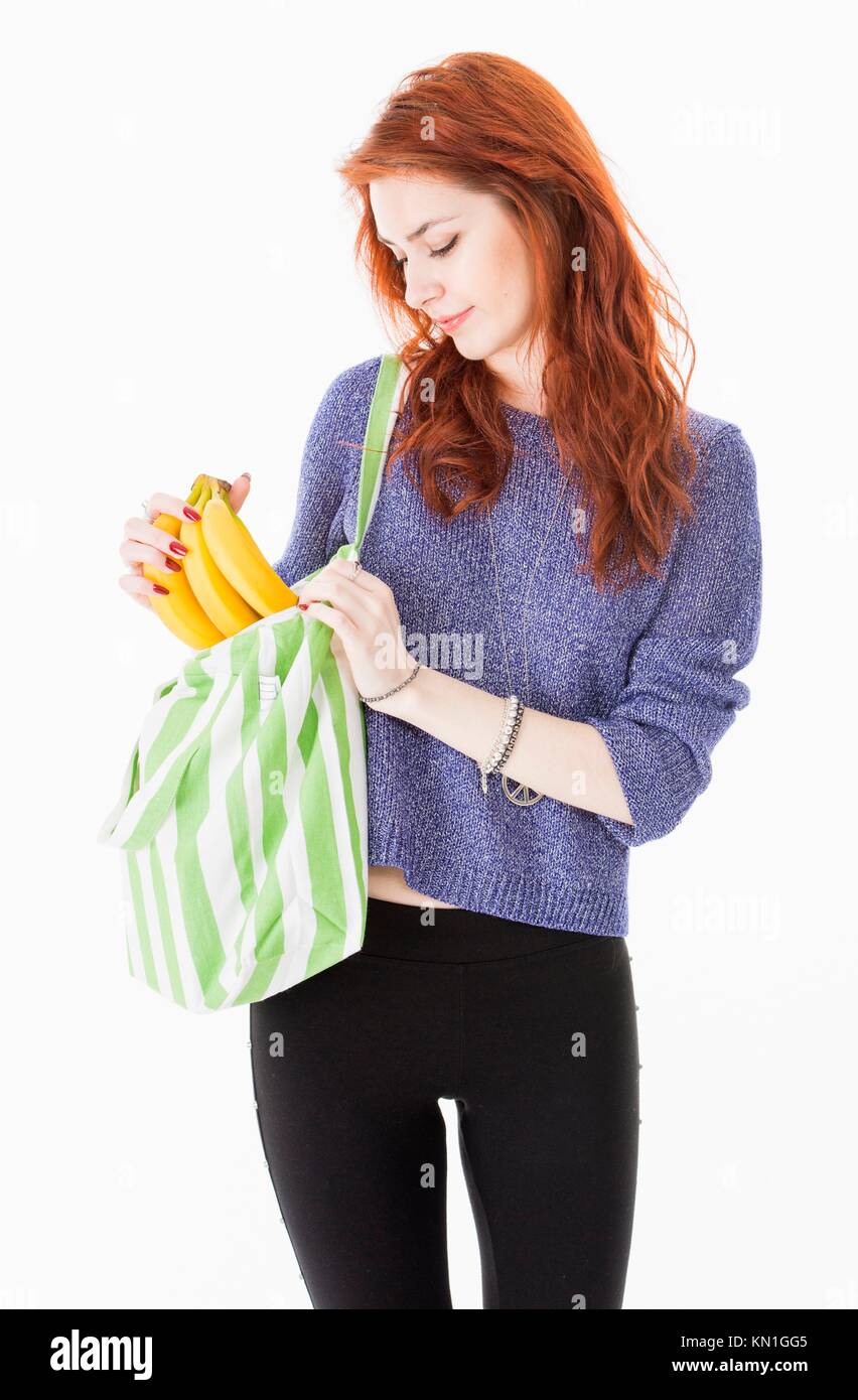Cheerful young woman putting bananas in reusable eco friendly shopping bag. Stock Photo