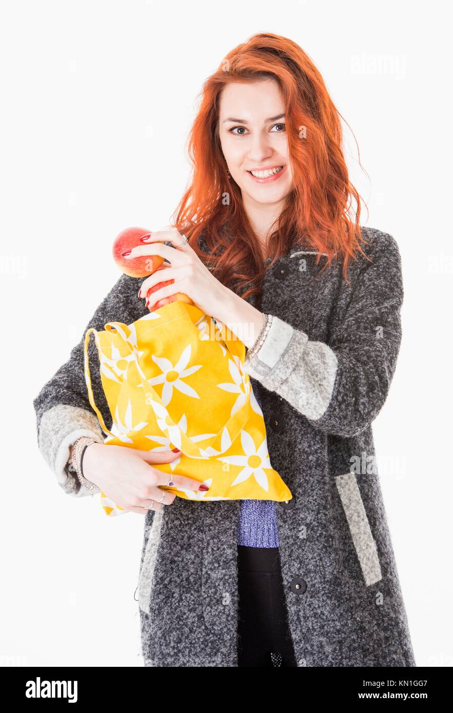 Cheerful young woman putting apples in reusable eco friendly shopping bag. Stock Photo
