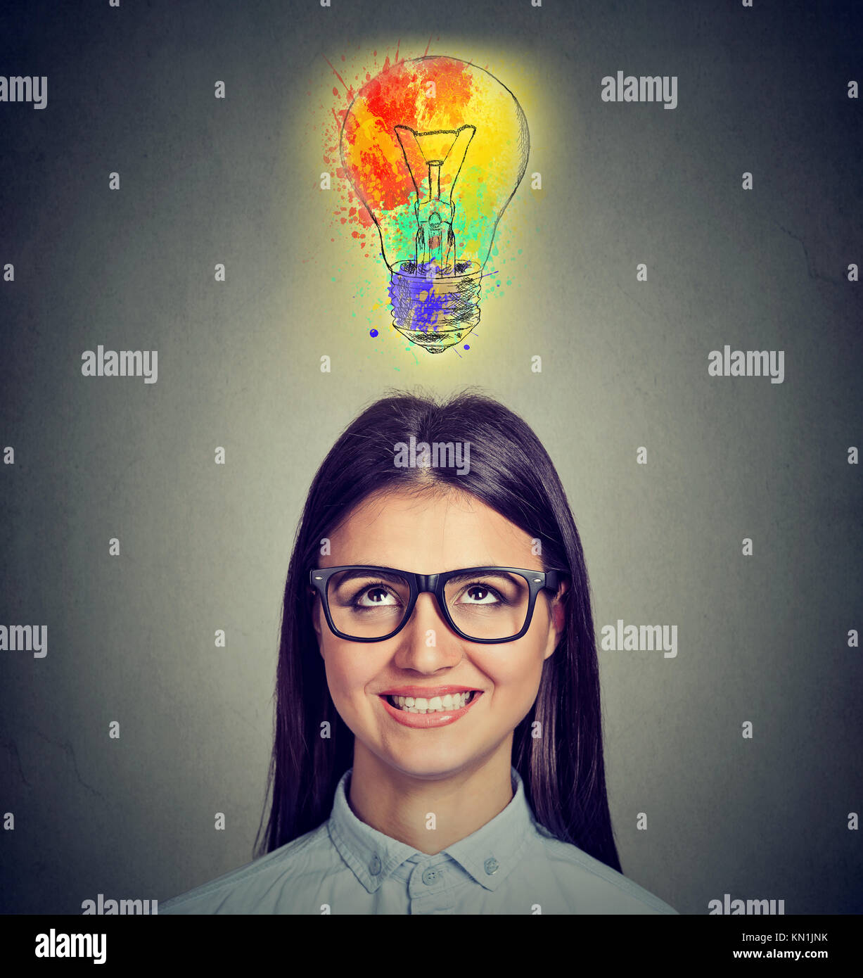 Portrait of a woman with glasses and creative idea looking up at colorful light bulb on gray background. Inspiration concept Stock Photo
