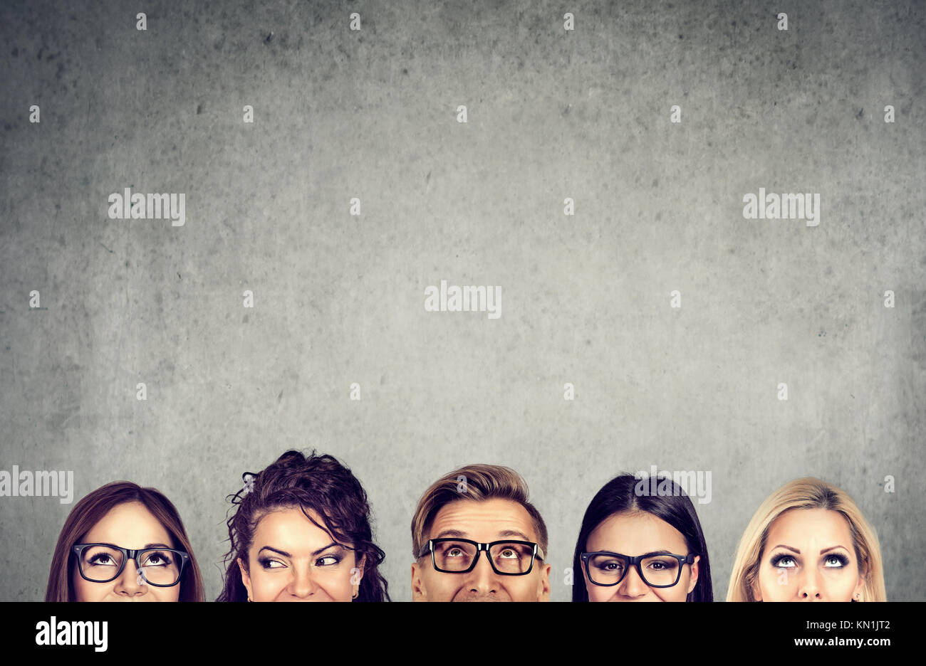 Closeup of young people heads standing near a gray concrete wall. A diverse business team and brainstorming concept Stock Photo