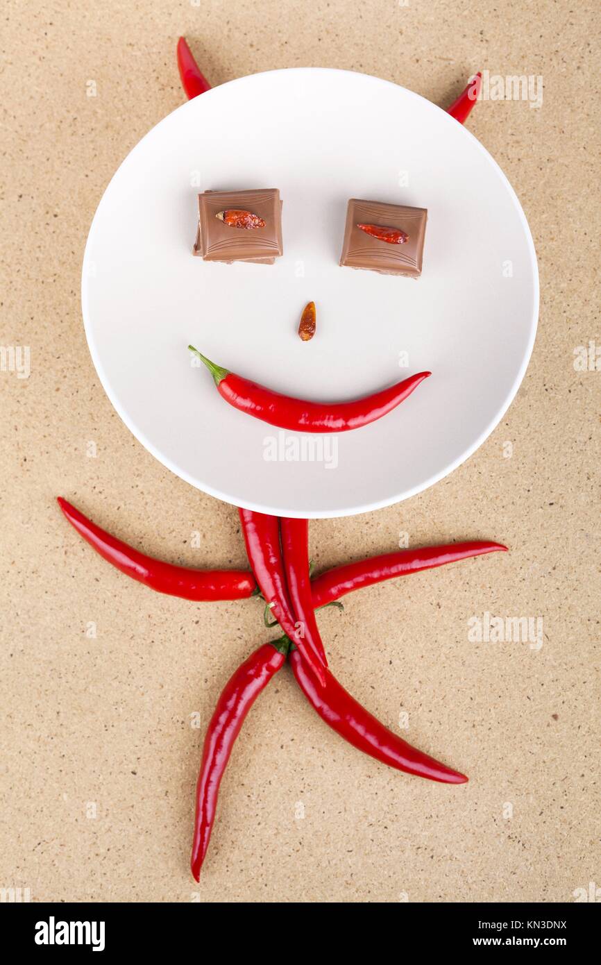 Happy chili pepper character with chocolate eyes on plate, over wooden