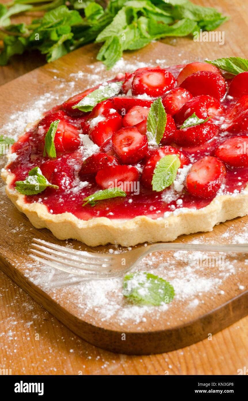 Delicious cream tart topped with fresh strawberries, mint and icing sugar. Stock Photo