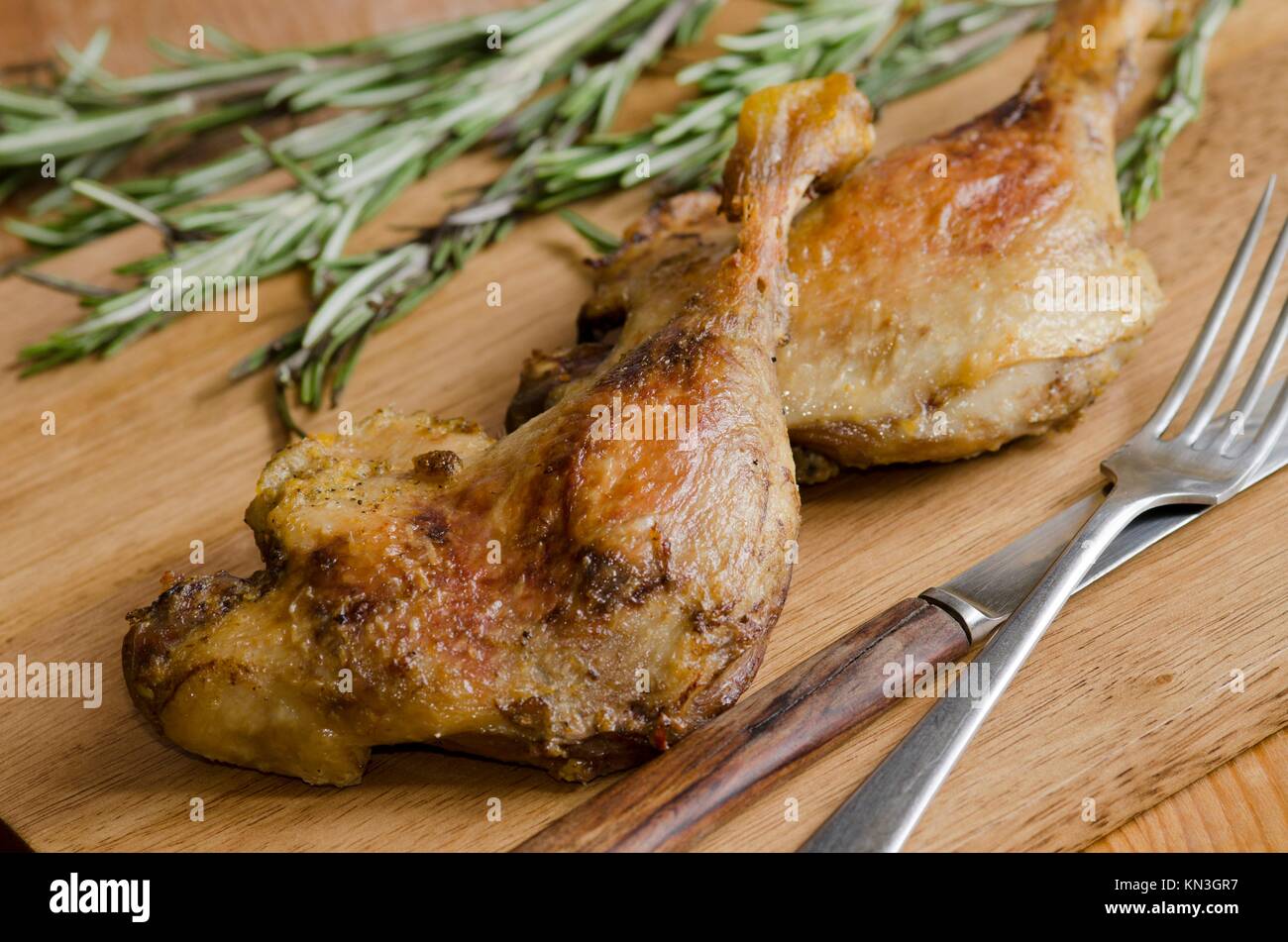Roast duck legs with rosemary on a wooden board. Stock Photo