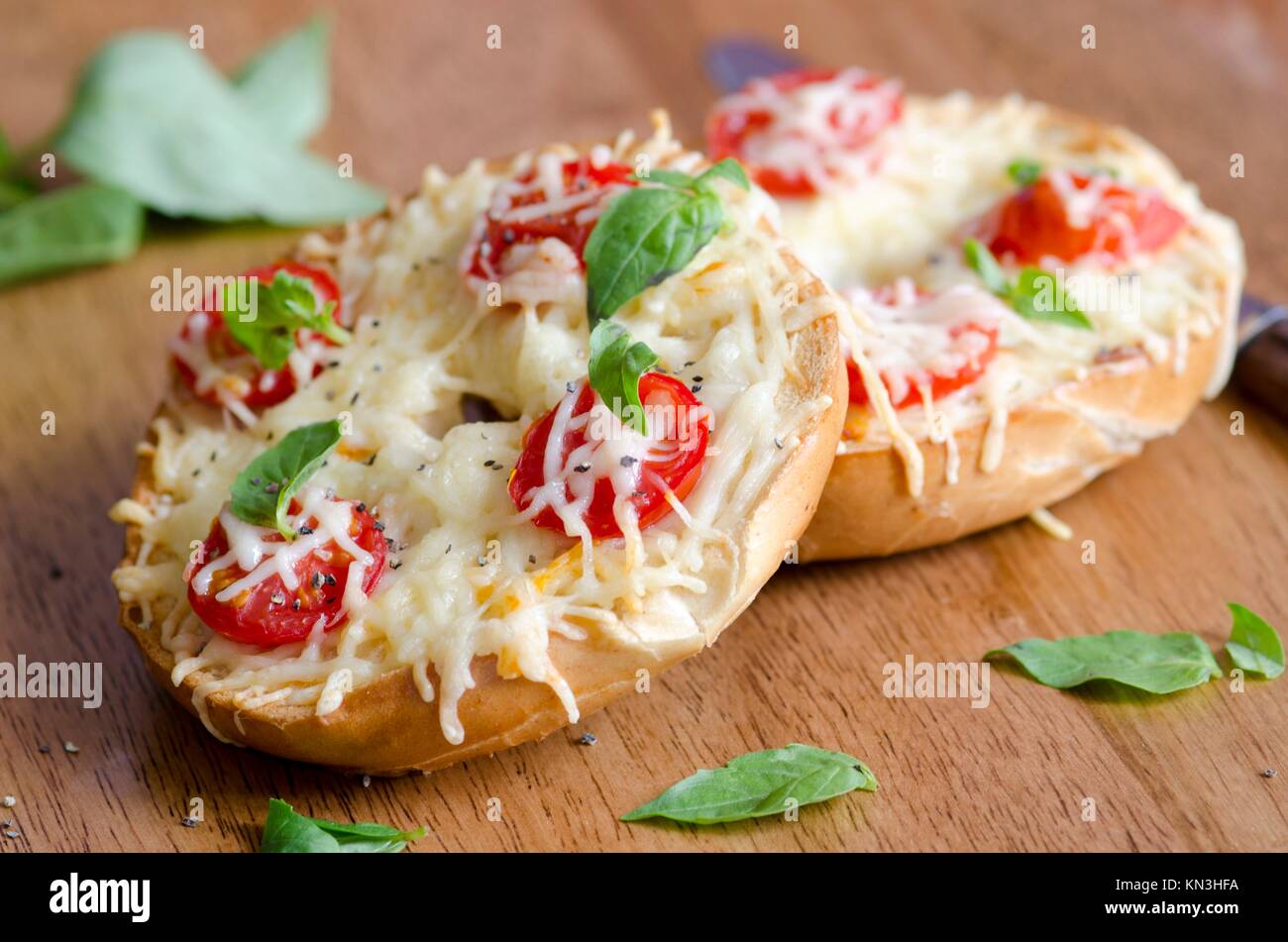 Bagels with melted cheese, cherry tomatoes and basil. Stock Photo