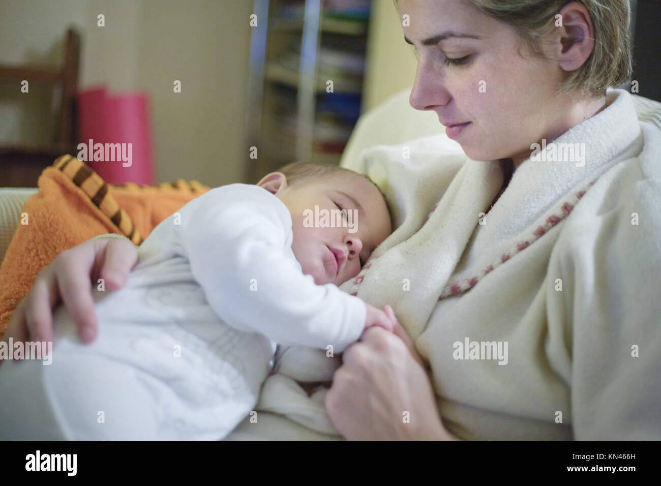 Mother holding sleeping 8 month old baby on sofa. Keeping silence. Stock Photo