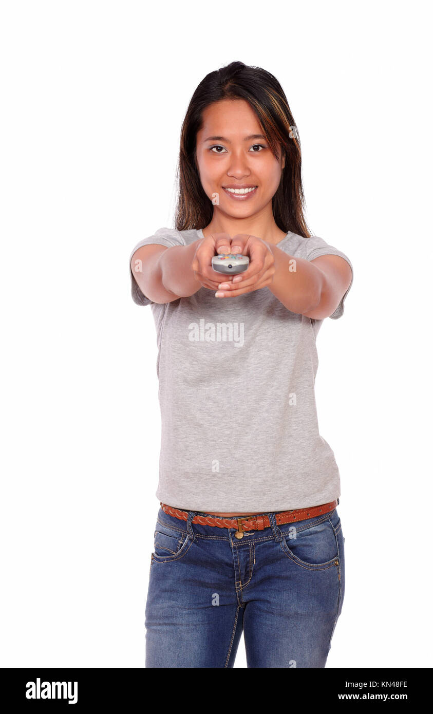 Portrait of an asiatic young female pointing at you with remote control against white background. Stock Photo