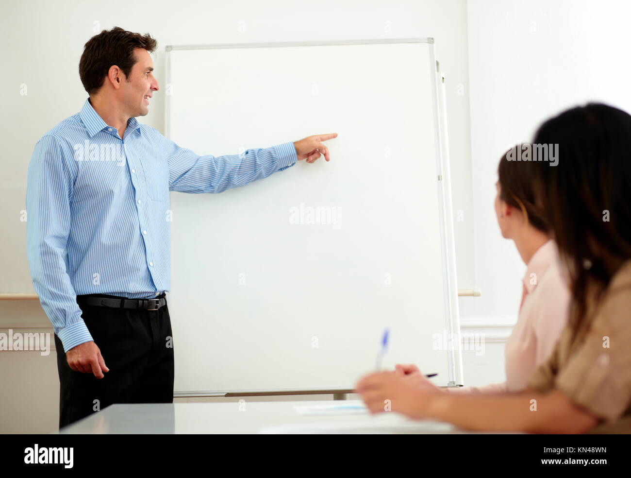 Portrait of a handsome adult businessman pointing and looking at whiteboard while standing in front of hispanic women on office - copyspace. Stock Photo
