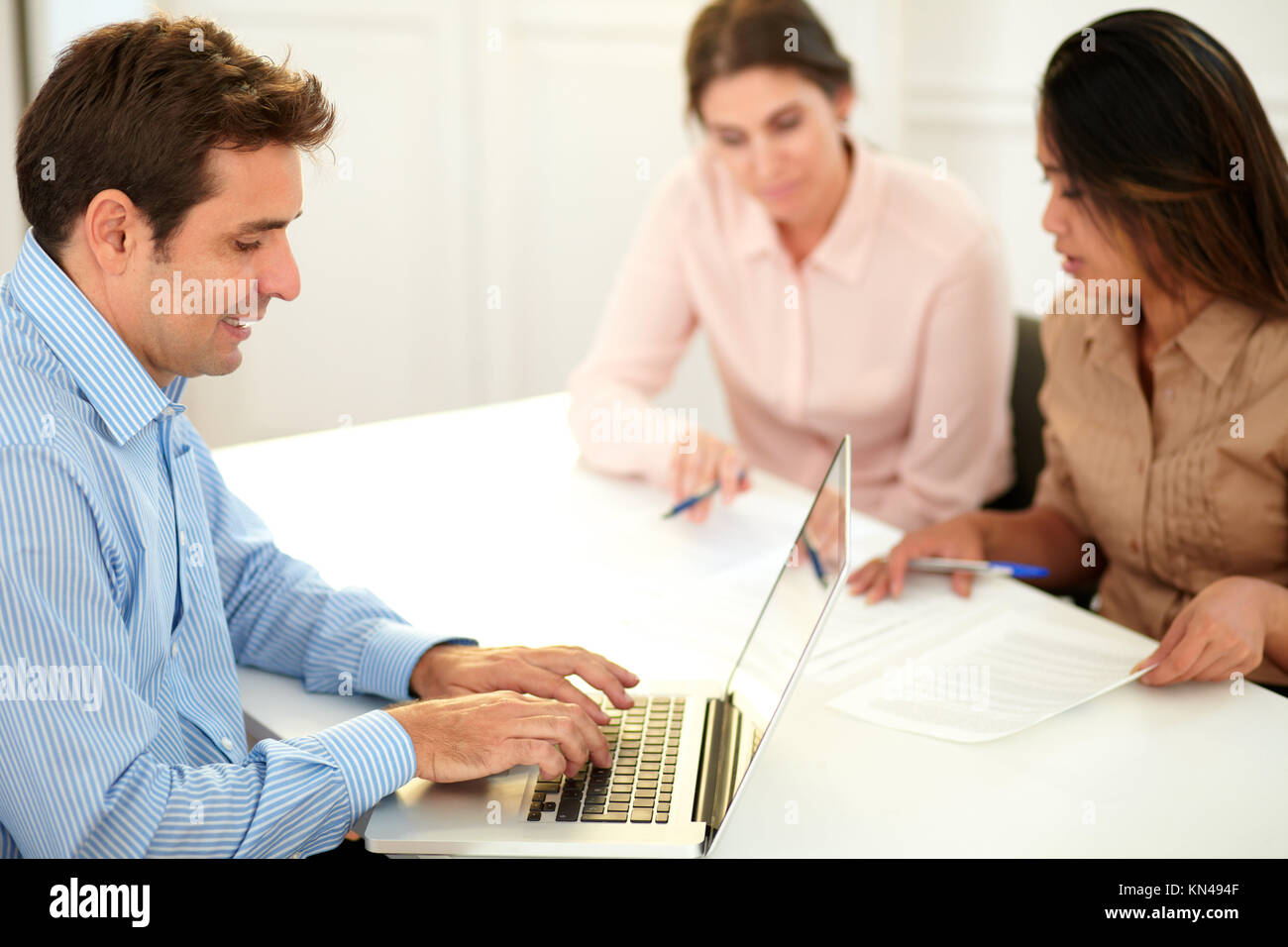 Portrait of adult hispanic businessman using his laptop while sitting in front of caucasian and asiatic women on office desk. Stock Photo