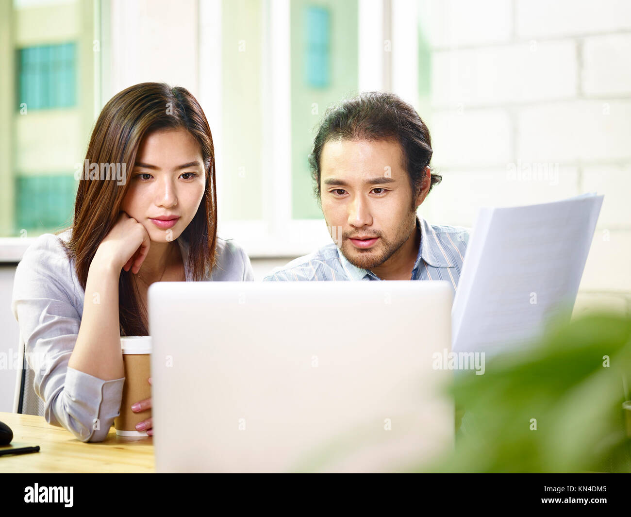 two asian corporate executives businessman and businesswoman working together in office analyzing a report using laptop computer. Stock Photo