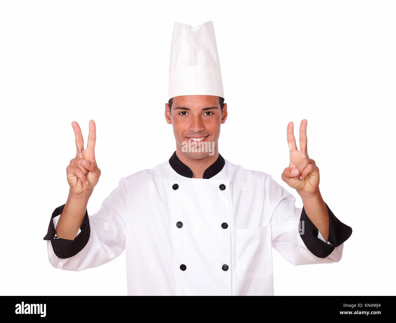 Portrait of professional 20-24 years male chef with victory fingers smiling at you while standing on isolated background. Stock Photo