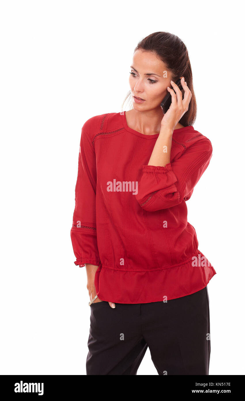Portrait of adult latin woman on red shirt talking on her cell while standing on isolated white background - copyspace. Stock Photo